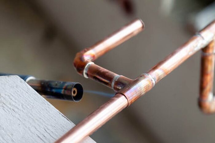 Skilled plumber soldering a copper pipe using a blow torch to ensure a secure and leak-free plumbing connection.